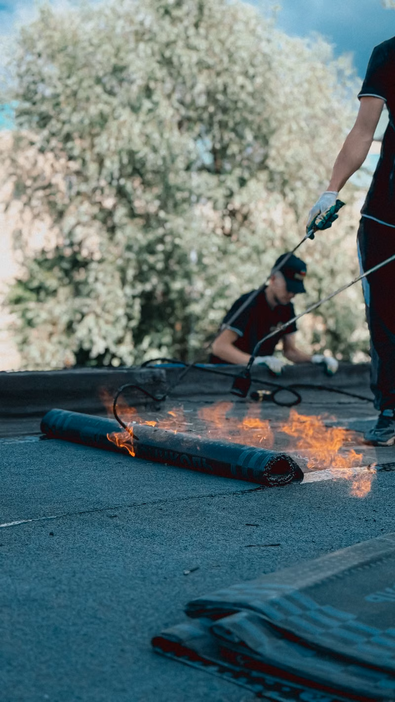 Roofers applying torch down rubber membrane for waterproofing. Outdoor construction scene highlighting skilled labor.